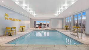 Un espace piscine intérieur moderne avec des murs en verre transparent, des chaises jaunes et un panneau indiquant : « J’ADORE L’AMBIANCE DE LA PISCINE ».