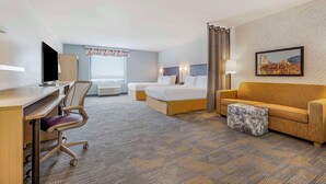 Une chambre d’hôtel équipée d’un bureau, de deux lits, d’un canapé et d’un petit pouf.