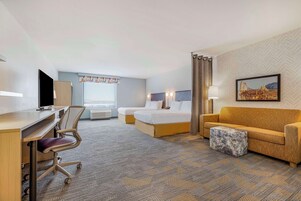 Una habitación de hotel con escritorio, dos camas, un sofá y un pequeño otoman.