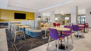 Un hall d’hôtel moderne, doté d’espaces aménagés avec des sièges, d’un téléviseur à écran plat et d’une cuisine en arrière-plan.