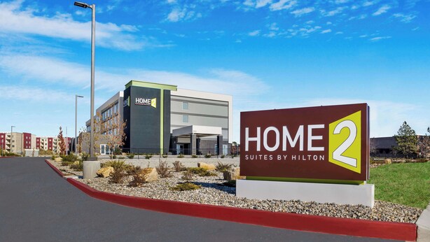 Un moderno edificio de hotel con un cartel que dice "HOME 2 Suites by Hilton" y un cielo azul despejado.
