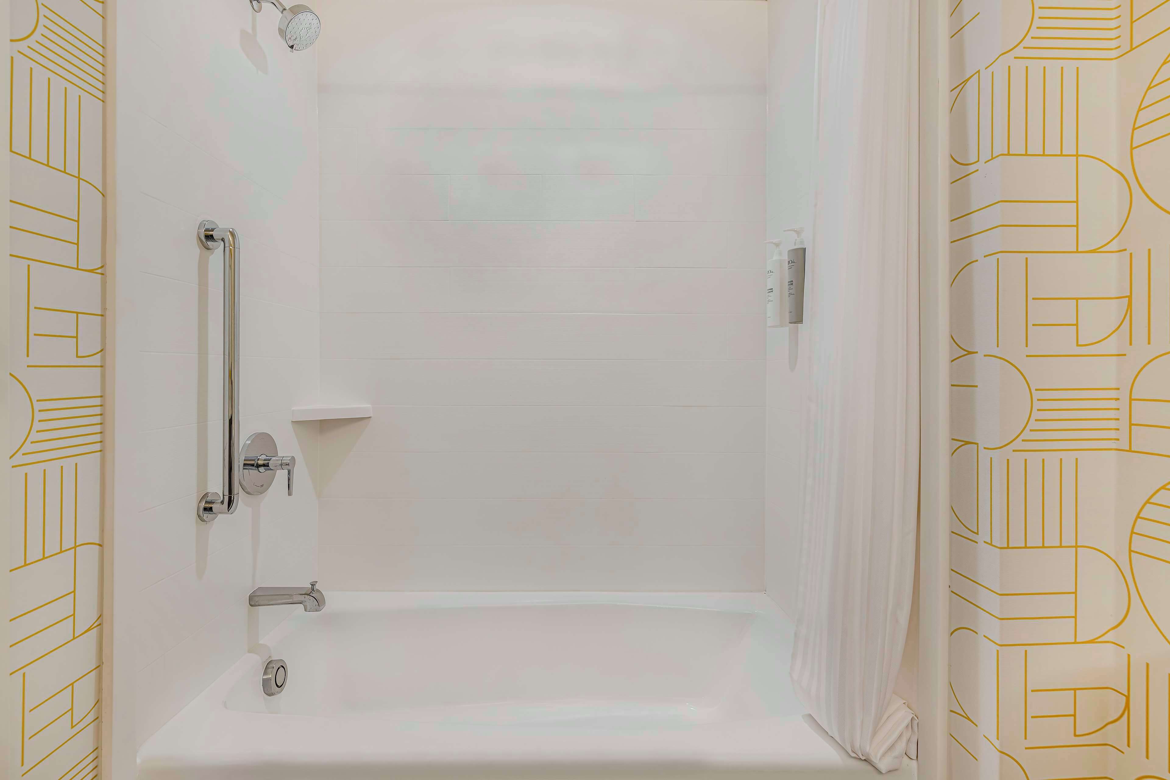 Un baño con una bañera blanca, ducha de mano y barra de apoyo.