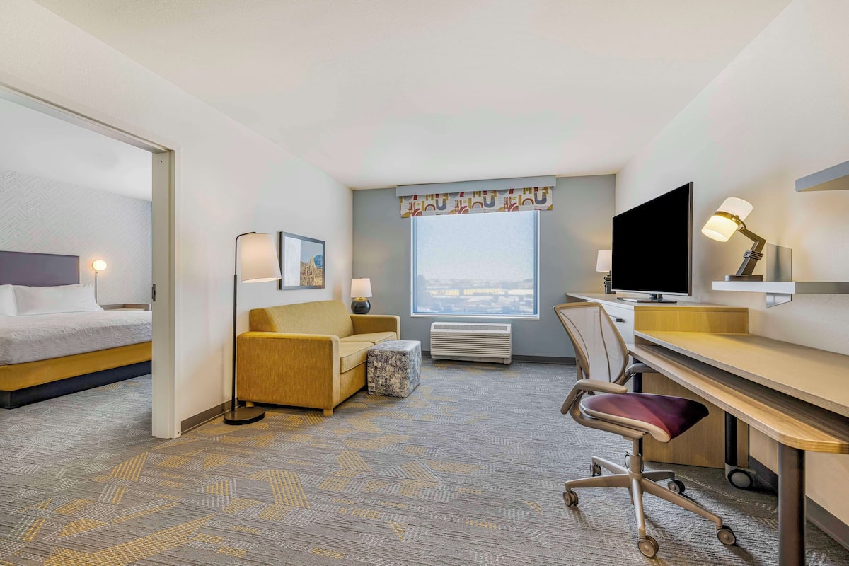 Une chambre d’hôtel comprenant un lit, un canapé, un bureau, une chaise, une télévision et une fenêtre donnant sur la ville.