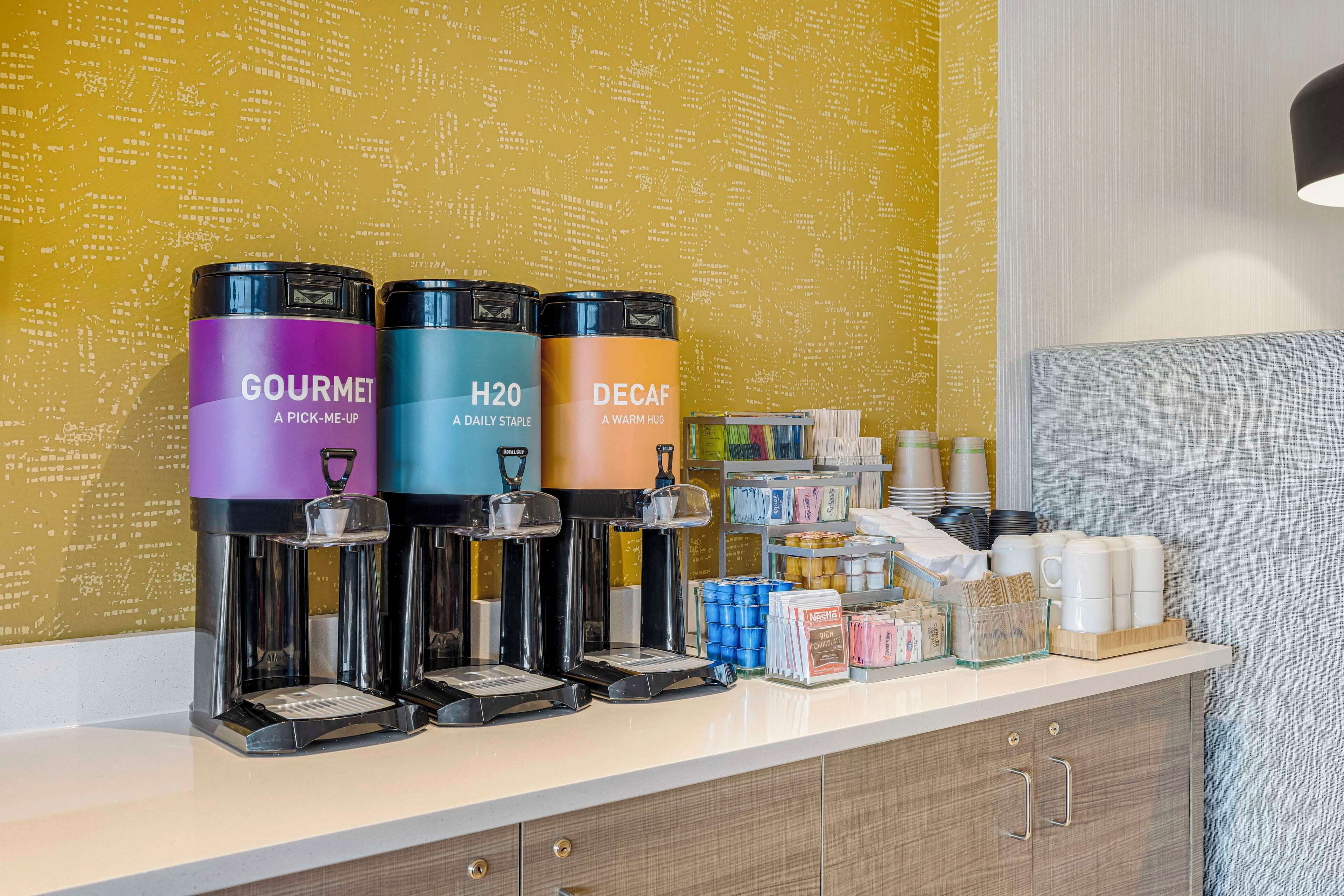 A coffee station with three dispensers labeled 'GOURMET,' 'H20,' and 'DECAF.'