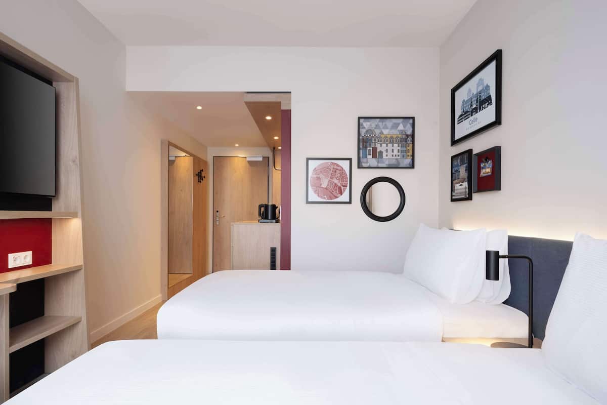 A hotel room with a bed, a TV, a coffee machine, and framed pictures on the wall.
