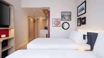 Habitación de hotel con una cama, televisor, cafetera y cuadros en la pared.