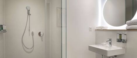 A modern bathroom with a glass-enclosed shower, a white sink, and a round mirror.