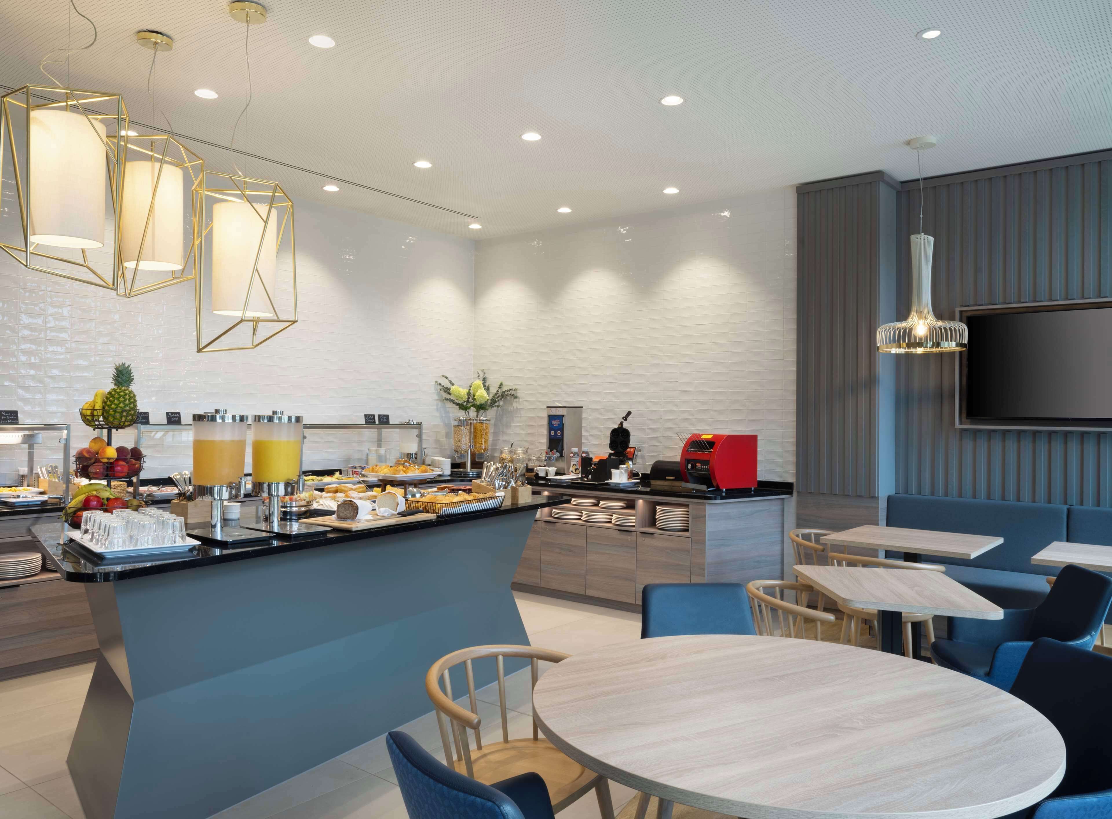A modern hotel lobby with a breakfast bar, seating area, and a TV mounted on the wall.