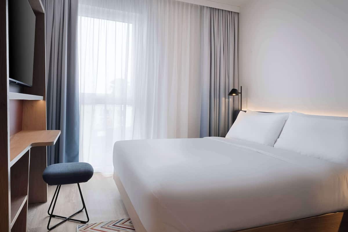 A modern hotel room with a large bed, a desk, a chair, and a TV.