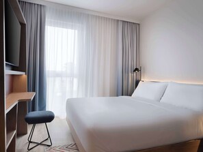 A modern hotel room with a large bed, a desk, a chair, and a TV. - Hampton By Hilton Celle (Celle)