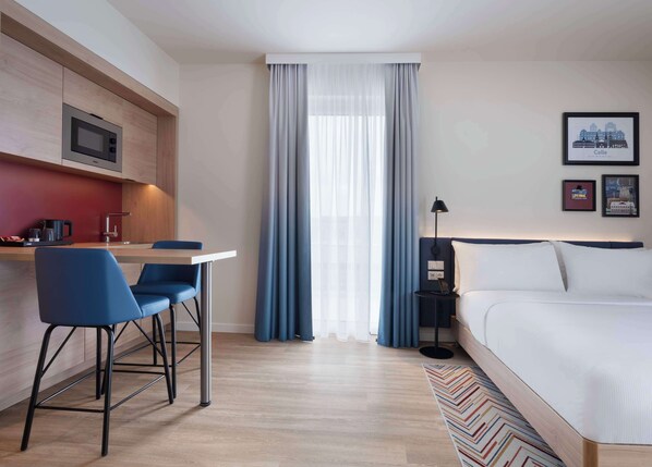 A hotel room with a bed, a desk with chairs, a microwave, a nightstand, and a window with curtains. - Hampton By Hilton Celle (Celle)