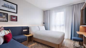 A modern hotel room with a bed, a sofa, a desk, and a TV.