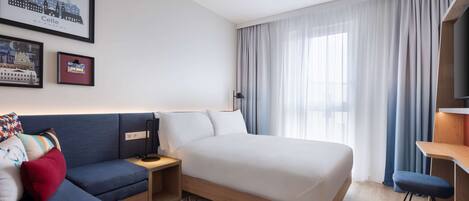 Una habitación de hotel moderna con cama, sofá, escritorio y televisor.