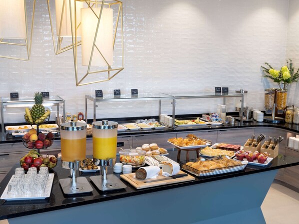 A buffet with various food items and drinks, including fruits, pastries, and beverages.