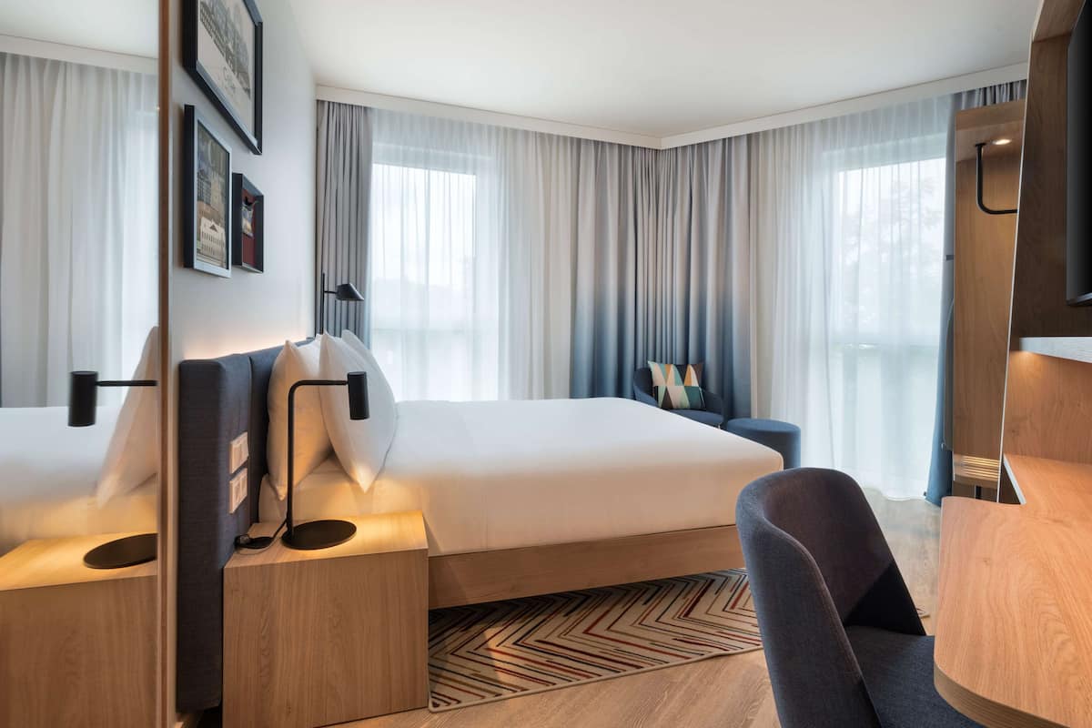 A hotel room with a large bed, a desk, a chair, and a TV.