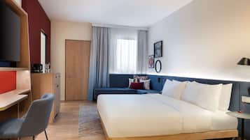 A modern hotel room with a large bed, a desk, a chair, and a sofa.