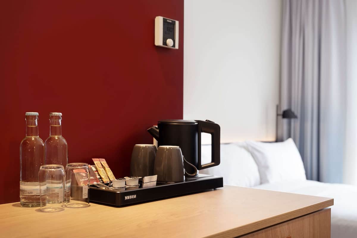 A hotel room with a wooden bedside table, a coffee maker, and three bottles of water.