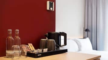 A hotel room with a wooden bedside table, a coffee maker, and three bottles of water.