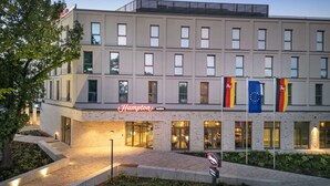 A modern hotel building with a sign reading "Hampton by Hilton" and flags of Germany, the EU, and the UK. - Hampton By Hilton Celle (Celle)