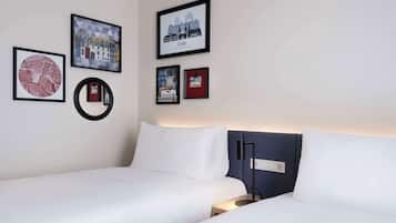 A hotel room with two beds, a round mirror, and several framed pictures on the wall.