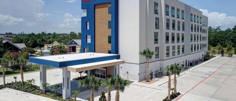A modern hotel with a prominent "Hampton Inn & Suites" sign, a covered entrance, and a parking lot with marked spaces.