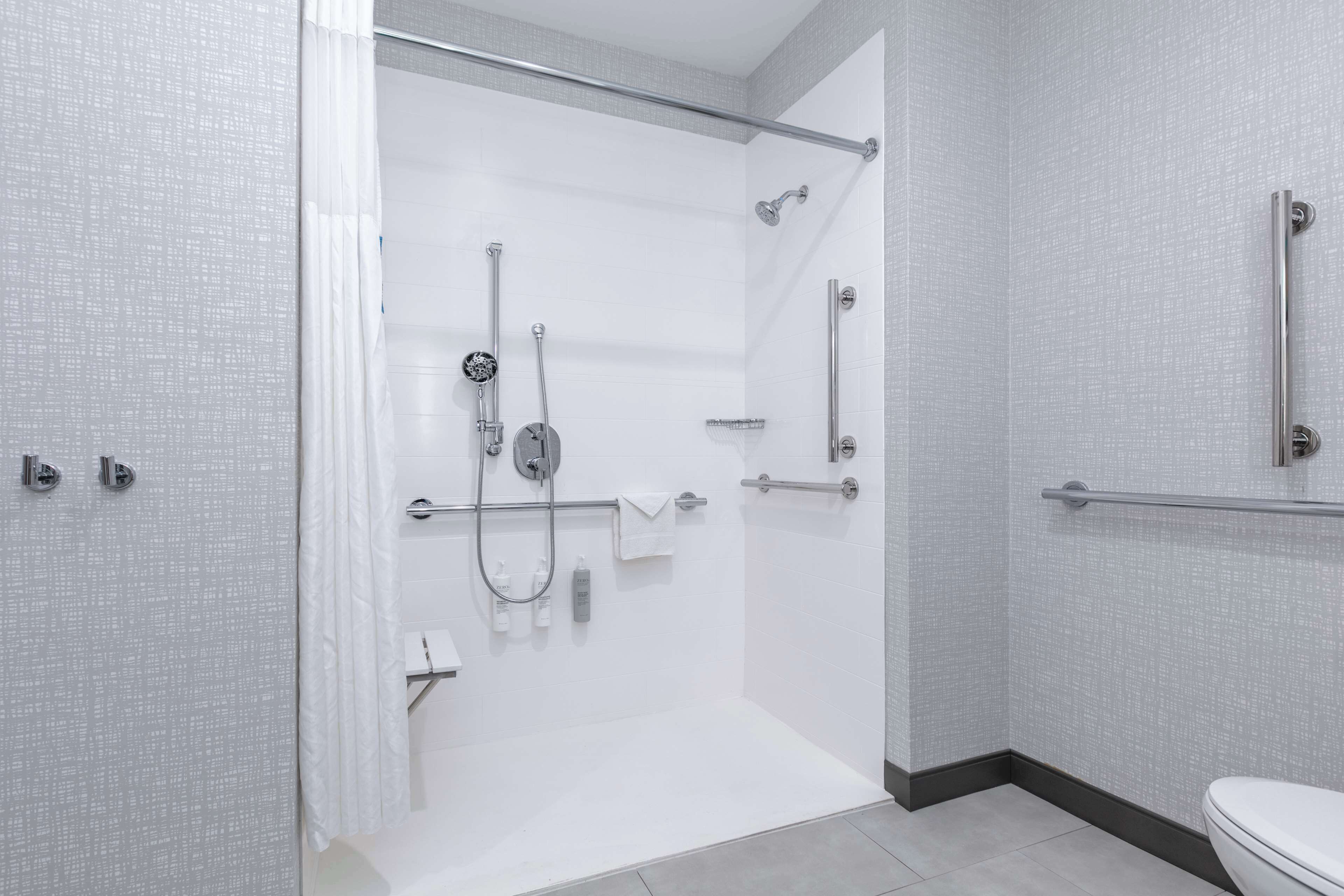 A modern bathroom with a walk-in shower, grab bars, and a toilet.