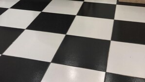 Quarto de hotel com cama, chão xadrez, parede de mármore e uma pequena área de banheiro.