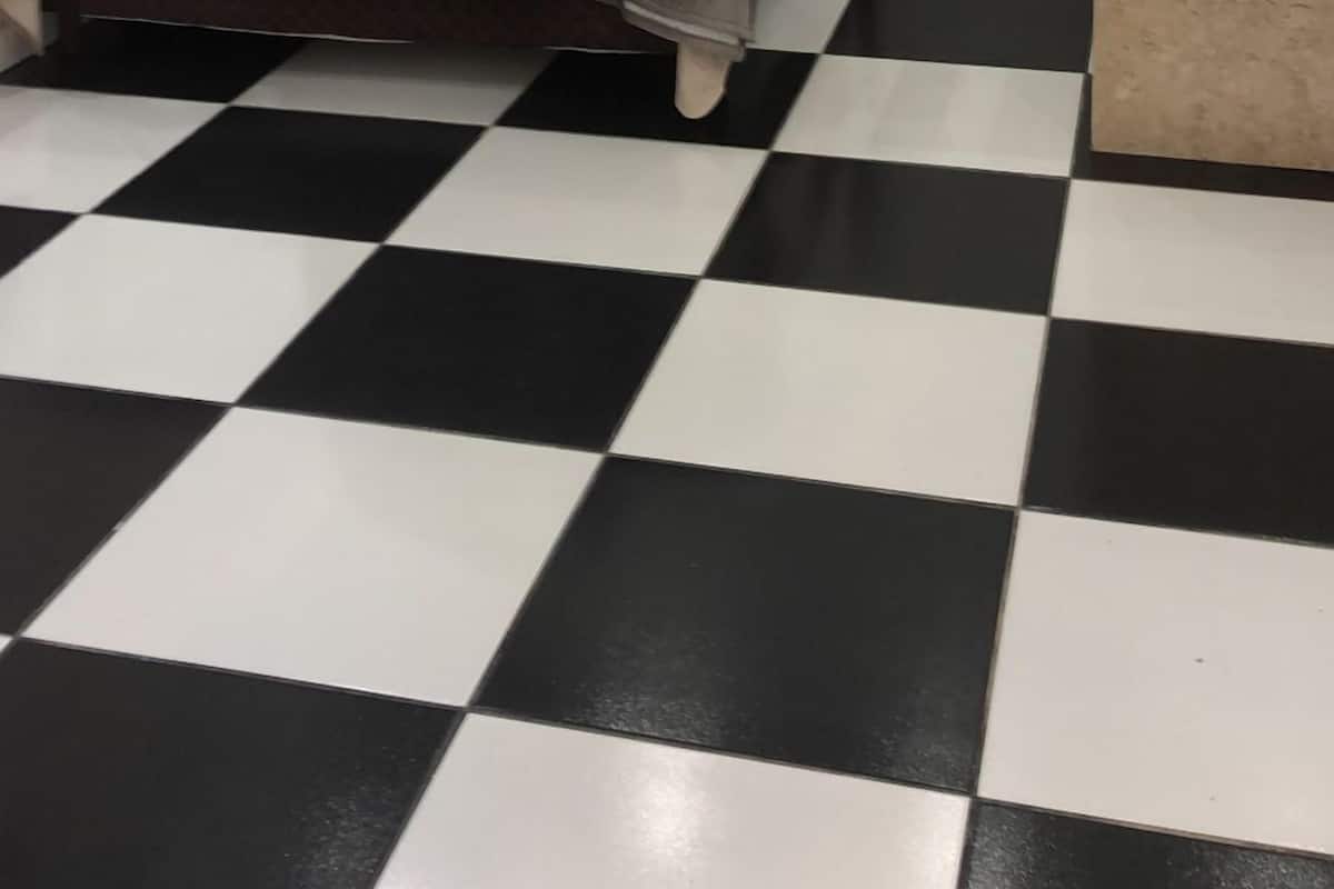 A hotel room with a bed, a checkered floor, a marble wall, and a small bathroom area.