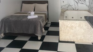 Quarto moderno com piso xadrez, cama com cobertor cinza, parede de mármore e uma banheira.