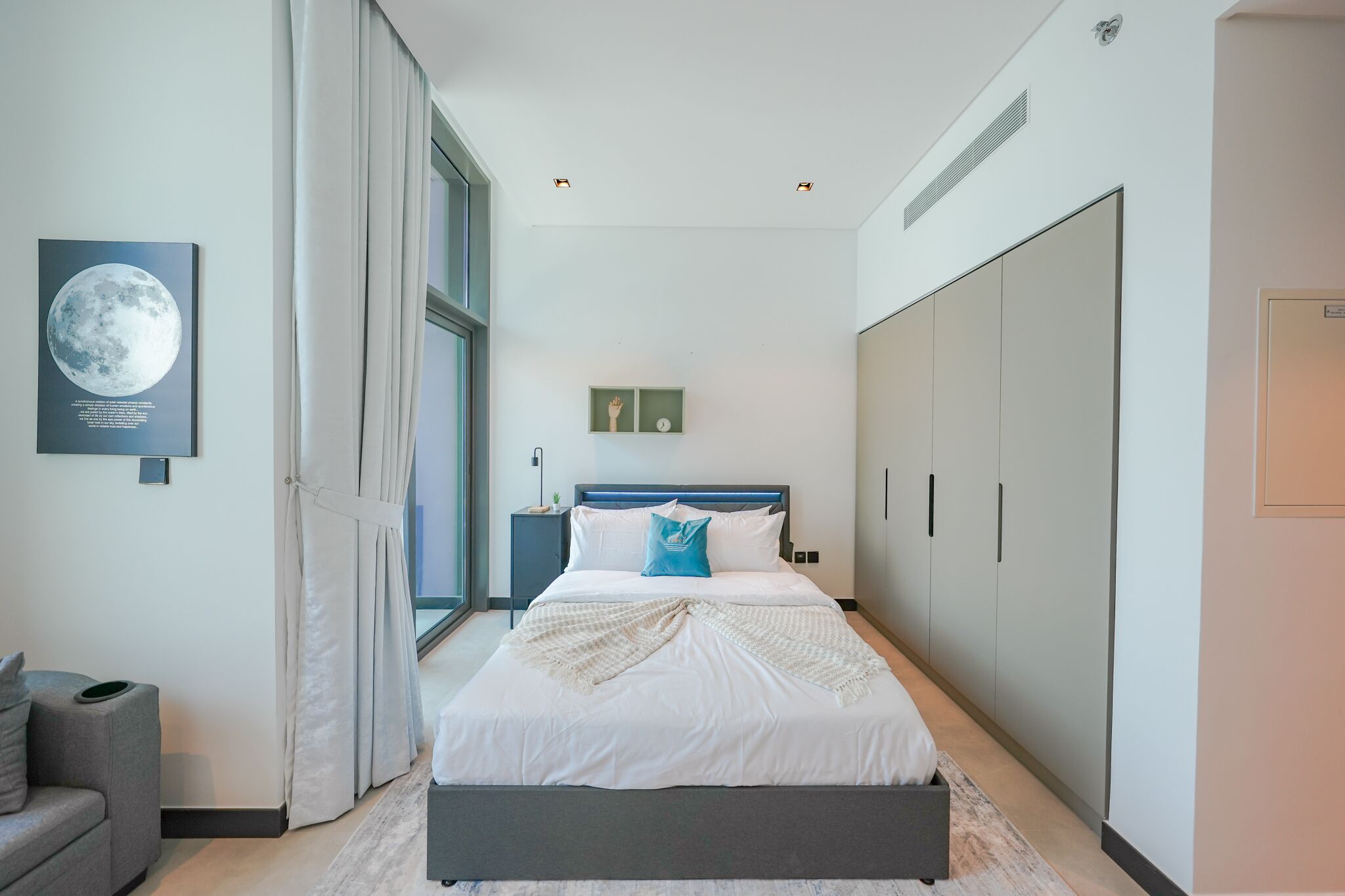 A modern bedroom with a large bed, a nightstand, a wardrobe, and a window with curtains.