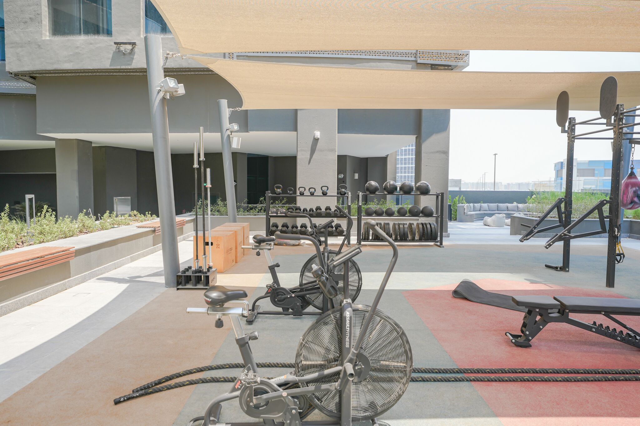 Uma área de ginástica ao ar livre com equipamentos de exercício, incluindo uma bicicleta ergométrica, pesos e um banco.