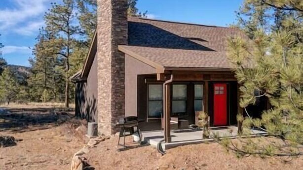 Une cabane rustique avec une cheminée, une porte rouge et une véranda.