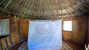 A room with a thatched roof, wooden walls, a bed with a white bedspread, and two patterned rugs on the floor. - Private waterfall and indigenous house! (Minca)