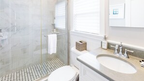 A modern bathroom with a glass shower enclosure, a toilet, a sink with a vanity, and a window with blinds.