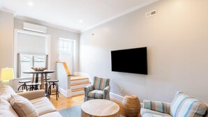 A modern living room with a sofa, a striped armchair, a round wooden coffee table, and a flat-screen TV mounted on the wall. - Two Level Condo with all the Essentials, Thames St (Newport)