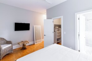 A bedroom with a bed, a television mounted on the wall, a wicker chair, a wooden table, and a wardrobe. - Two Level Condo with all the Essentials, Thames St (Newport)