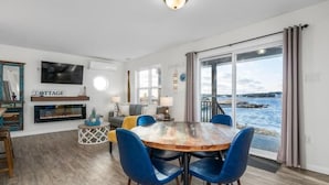 Una sala moderna con chimenea, un comedor con sillas azules y un ventanal con vista al agua.