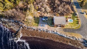 Vista aérea de una propiedad costera con una pequeña casa, una piscina y un litoral rocoso.
