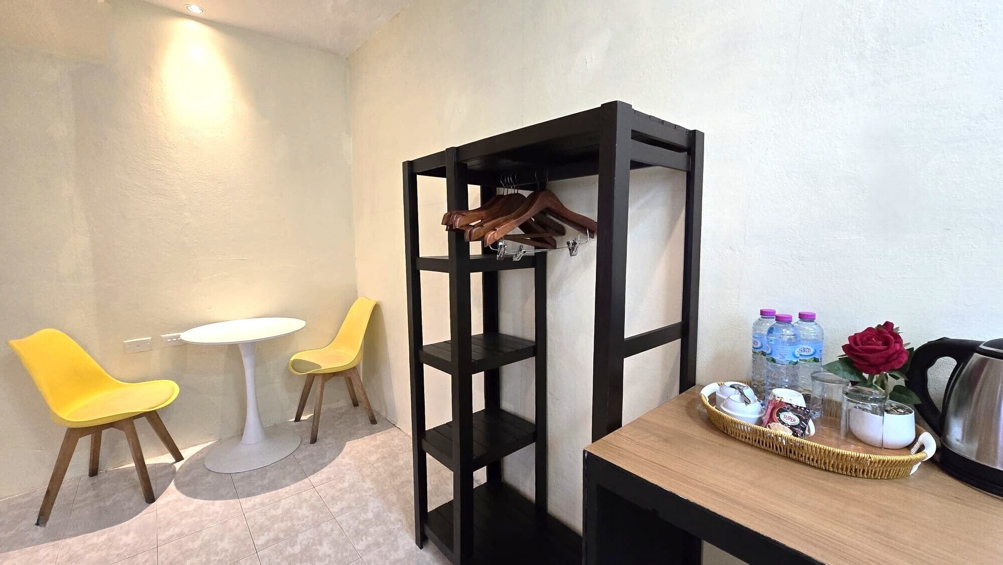 A room with a wooden table, two yellow chairs, a white round table, and a black shelving unit with a hook.