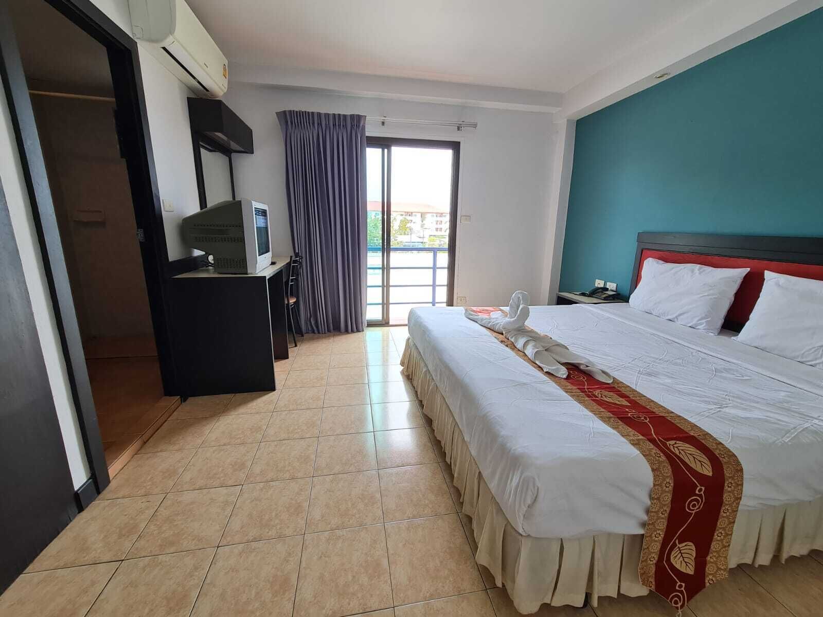 Habitación de hotel con cama, escritorio con computadora, ventana con cortinas y vista al exterior.