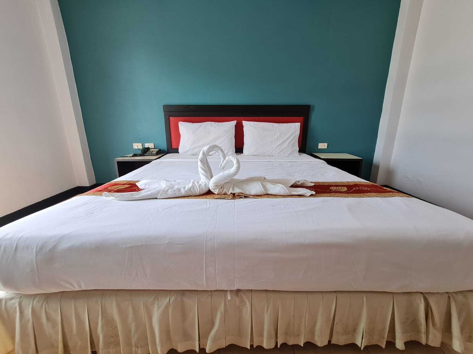 A neatly made bed with a swan-shaped towel arrangement, a red headboard, and a teal wall.