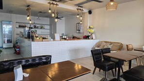 Interior de un restaurante con barra, diferentes disposiciones de mesas y un mostrador con diversos artículos.
