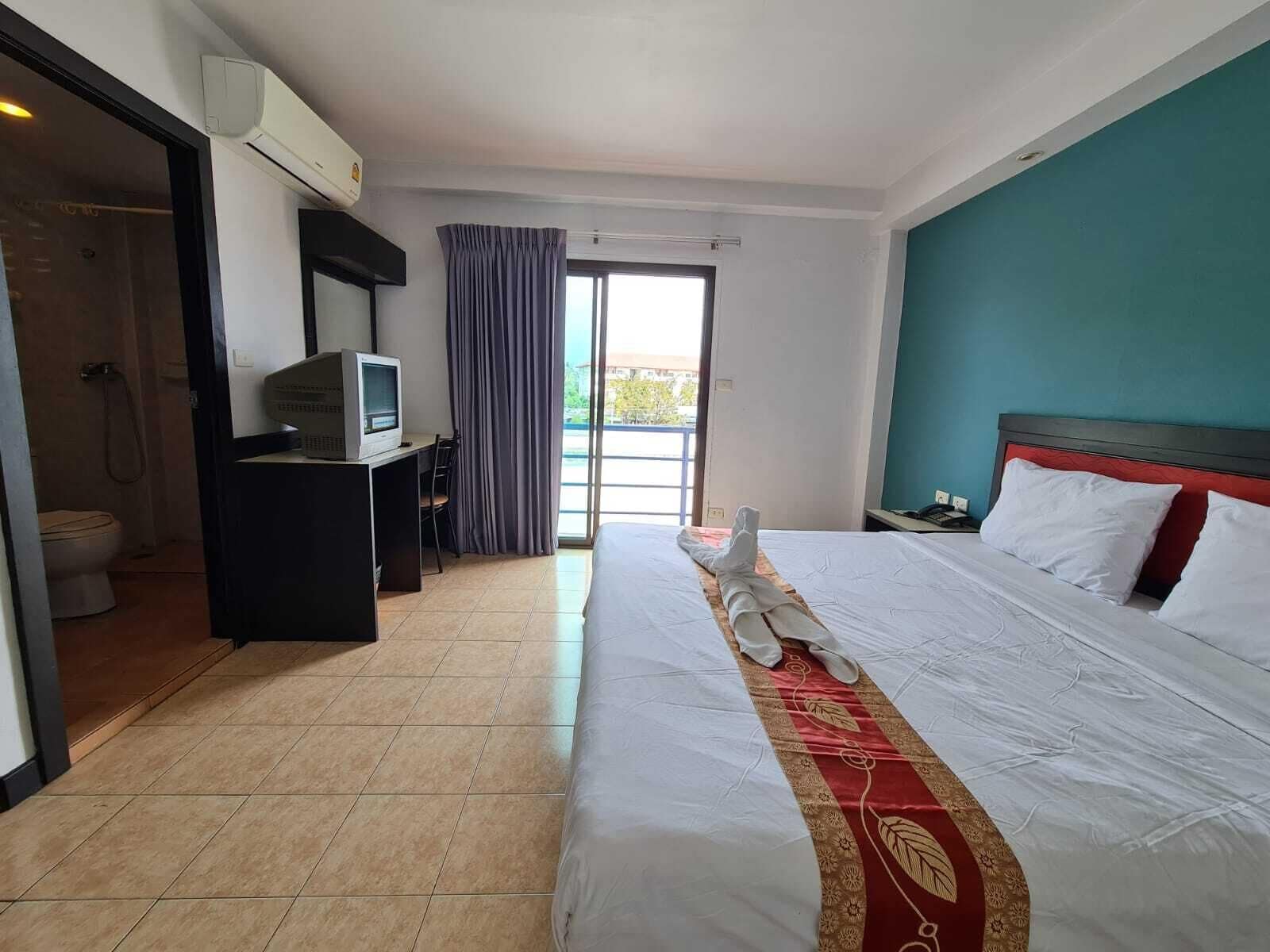A hotel room with a bed, a desk with a computer, a television, and a view of the outdoors.