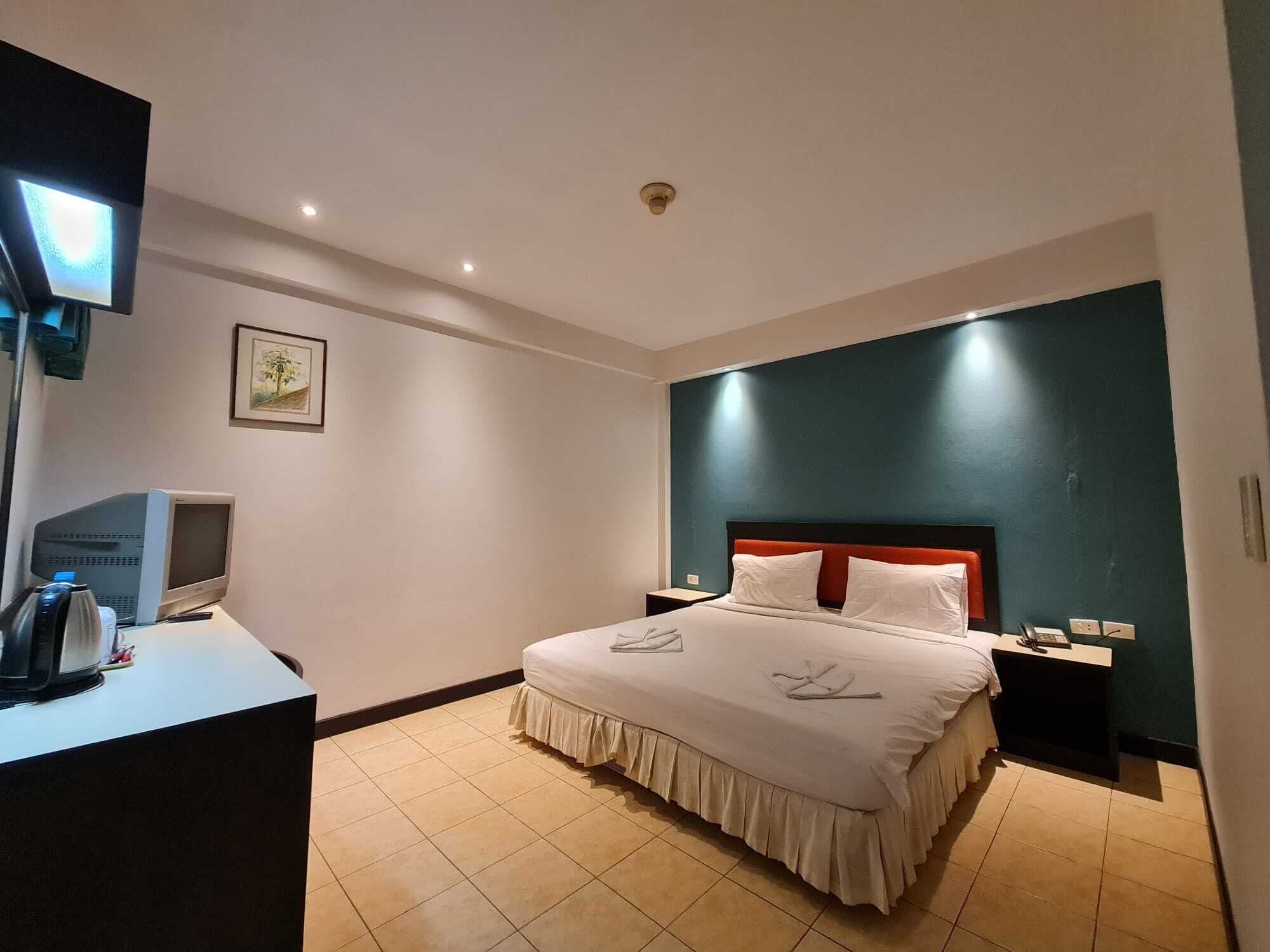 A hotel room with a bed, bedside tables, a desk with a computer, and a television.