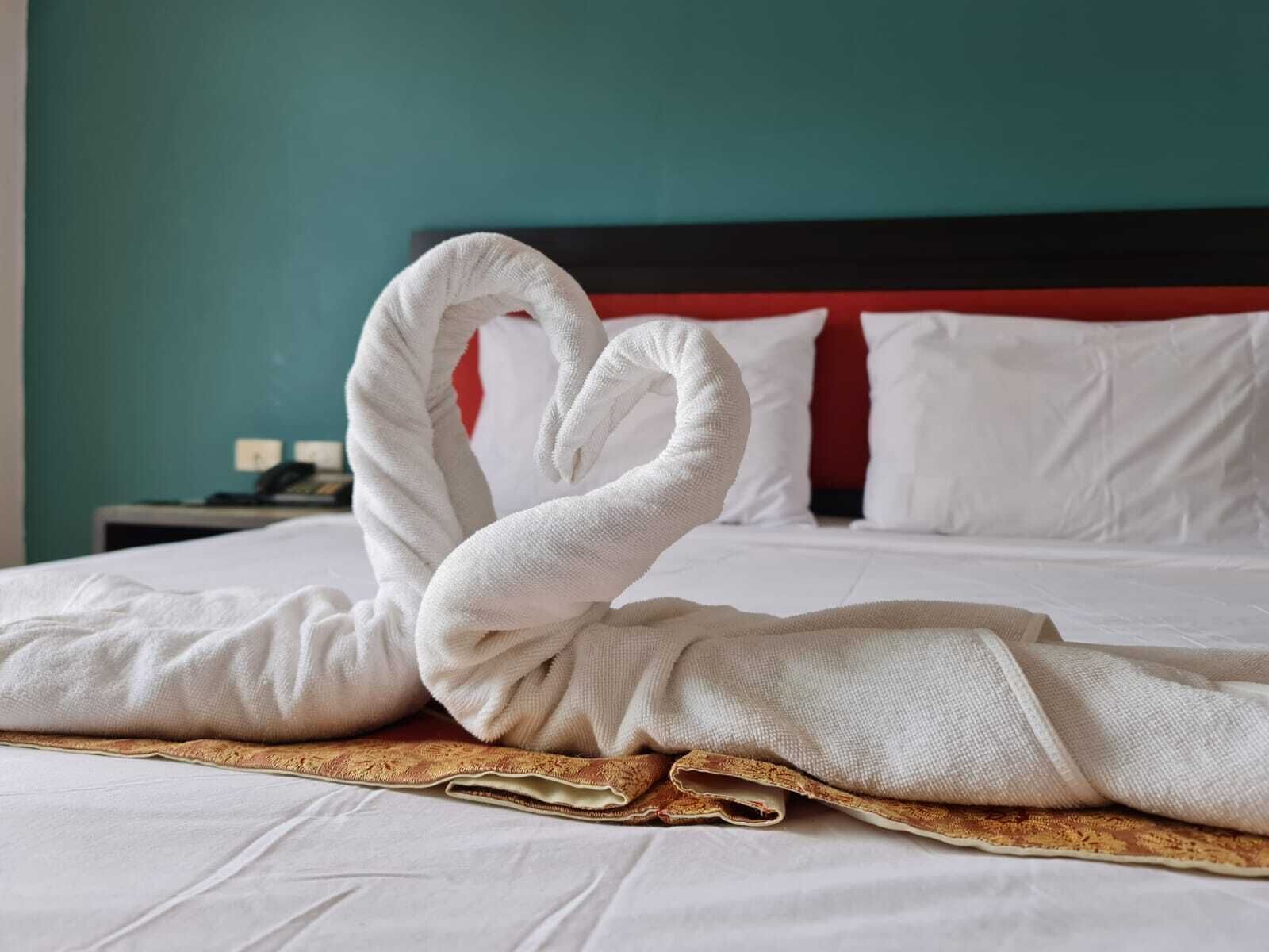 Un letto rifatto con cura, coperto da una coperta bianca e decorato con un elegante componimento di asciugamani a forma di cigno.