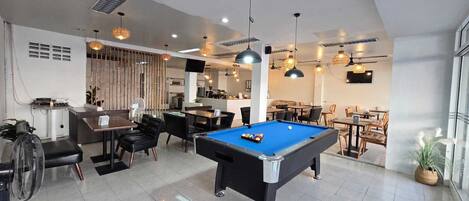 A modern indoor space with a pool table, dining area, and kitchen.
