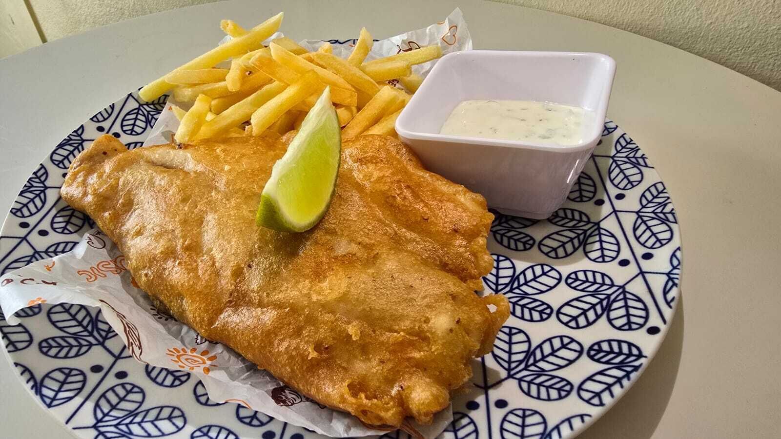 Un plato con un filete de pescado, papas fritas y un recipiente pequeño con salsa.