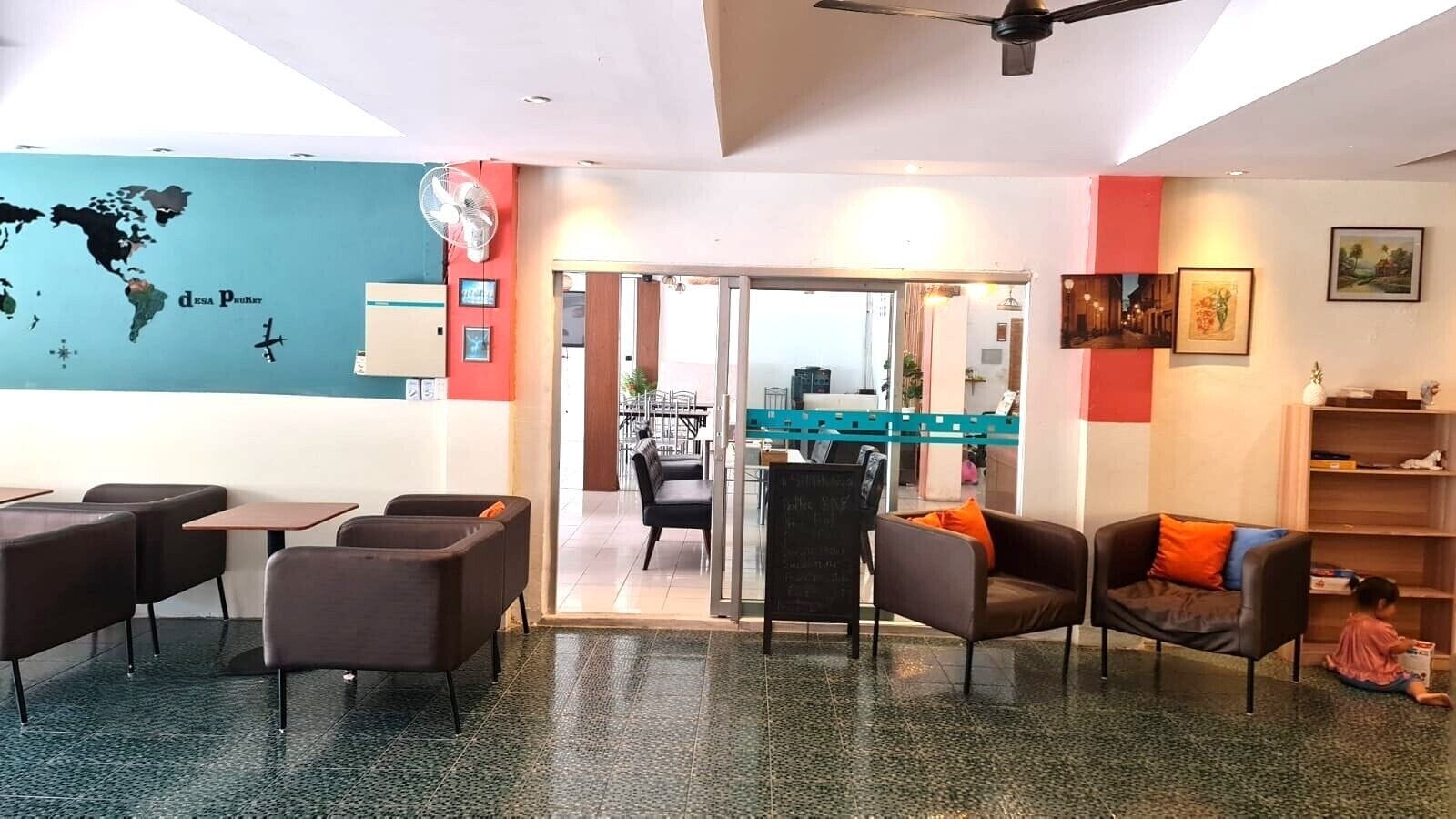 Vestíbulo de hotel con zonas de estar, un mapa mundial en la pared, un ventilador y un niño jugando.