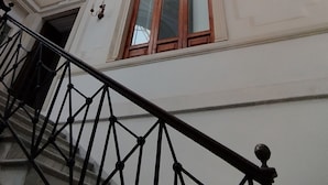 Eine prächtige Treppe mit schwarzer Balustrade führt zu einem Raum mit einem großen, runden Buntglasfenster.