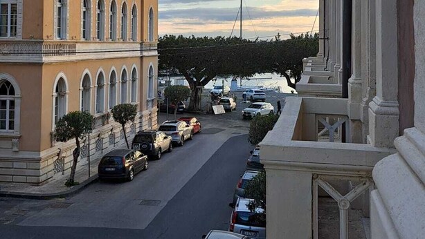 Straßenansicht mit geparkten Autos, einem Gebäude mit Rundbogenfenstern und einem klaren Himmel.